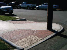 Photo shows paired perpendicular curb ramps. One side has a returned edge – good for wayfinding -- against a planting strip; the other side is flared.