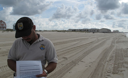 A man in USFWS clothing looks at data on the beach