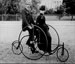 Smartley dressed couple seated on a 1886-model bike for two
