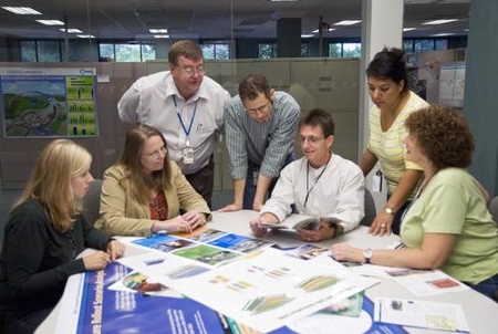 Photograph of several adults gathered around a table studying energy-related printed materials.