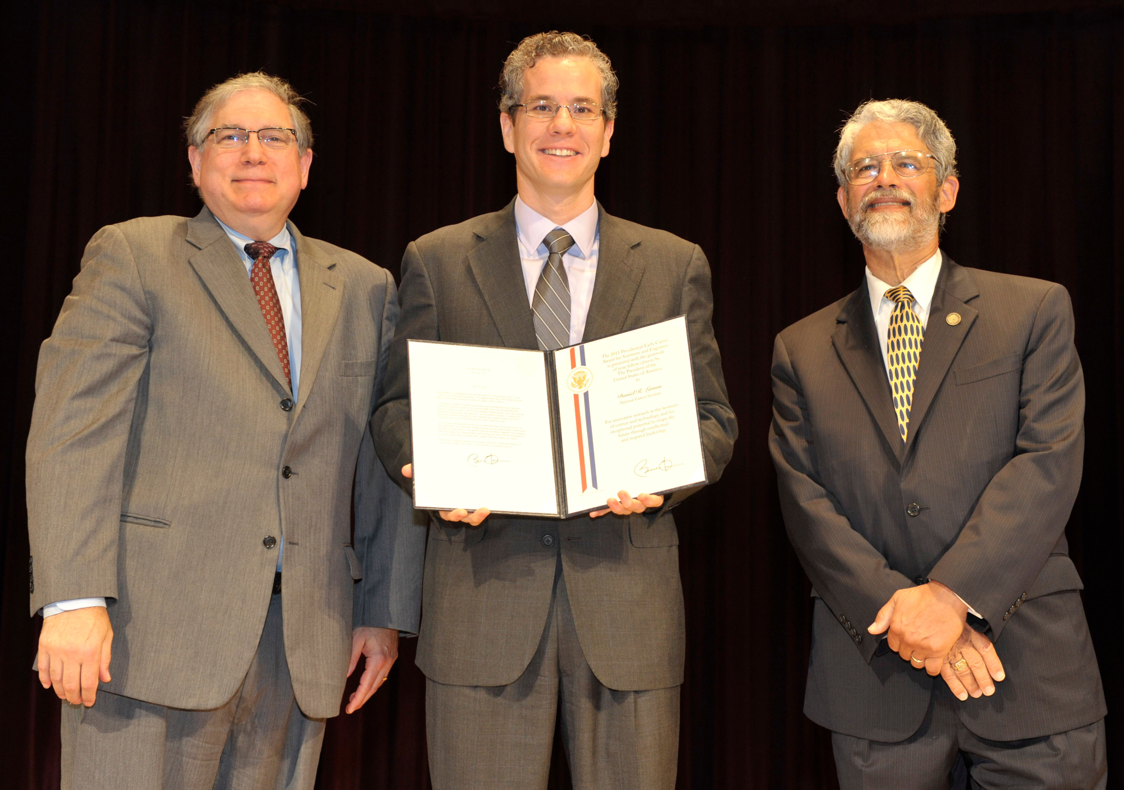 Dr. Larson stands between Dr. Tabak (left) and Dr. Holdren (right), while holding his award 