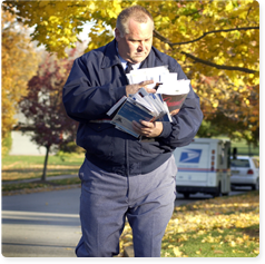 A mail carrier walking down the street sorting through a large pile of letters he is holding