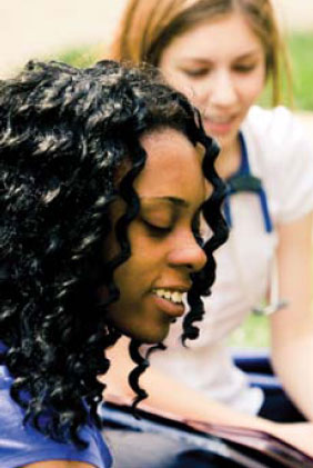 This photo shows a 17-year-old African American young woman smiling in the foreground and a Caucasian nurse in the background. 