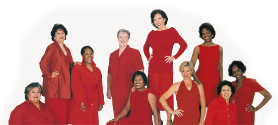Grupo de mujeres sentadas y de pie con vestidos rojo.