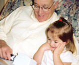 Man using a vision device to read as a little girl watches.