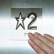 A woman's hand, reading the braille floor designation by an elevator button