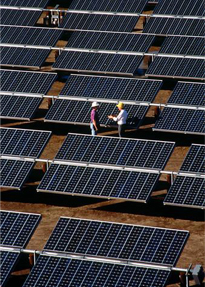 Photo of two men in hard hats talking among multiple rows of photovoltaic arrays.