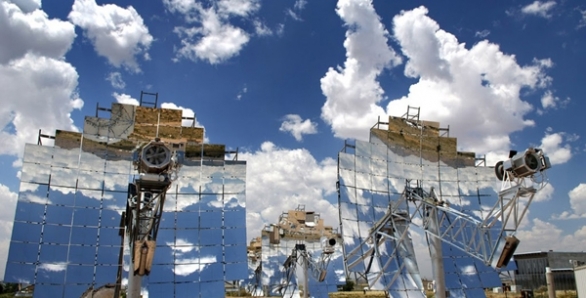 Photo of 3 solar dishes, which have reflective, square-shaped material that creates a mirror image of the sky and clouds. Each dish is anchored to the ground by a vertical pole.