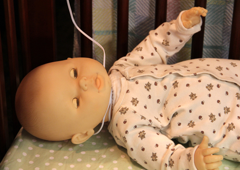 Baby doll in a crib with a baby monitor cord wrapped around its neck