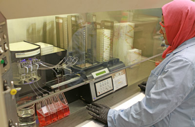 Lab technician under a hood, using device that loads plates with cell cultures