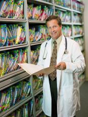 Photograph of a doctor holding a patient's records with a wall of records in the background