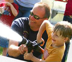 A firefighter helps a young boy hold a fire hose
