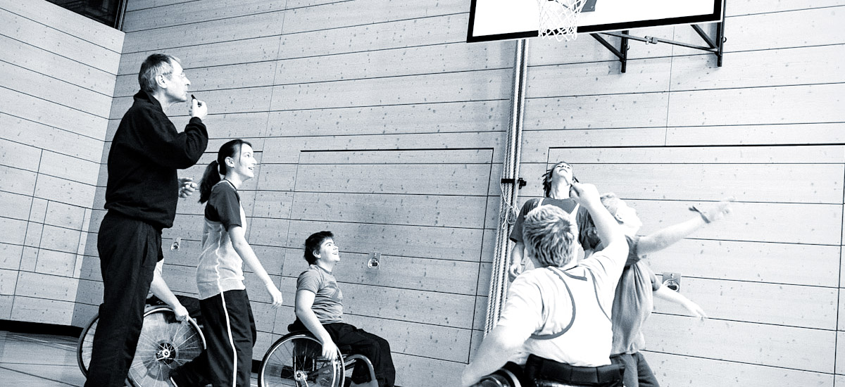 Photo of kids in wheelchairs playing basketball while coach blows whistle