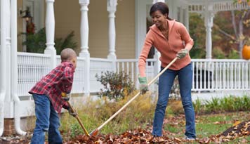 Photo of a mom and her little girl raking leaves into a pile