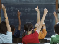 group of children in a classroom with their hands raised