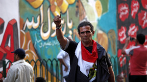 An Egyptian man waves an empty bullet case in front of a mural that was painted on a recently whitewashed wall in Tahrir Square, Cairo.