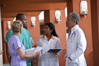 Image: Photo of a four-member health care team having a discussion in a hospital hallway.