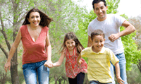 Two smiling parents are running playfully outside with their young son and daughter.