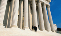 Three people in black suits are walking up the steps of the U.S. Supreme Court building in Washington, DC.
