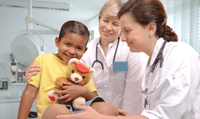 Two female physicians in lab coats are smiling and caring for a young male patient. 