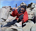 Photo - Person on mountain with rock hammer. Click for credit.