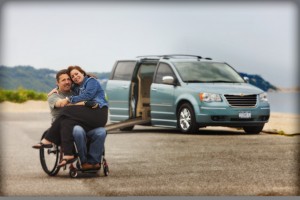 Photograph of a man in a wheelchair, with a woman sitting on his lap, and a van with a ramp in the background