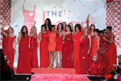 17 celebrity women from The Heart Truth's 2010 Fashion Show wearing designer red dresses laughing and waving to the audience at end of the 2010 fashion show. They are standing in front of a large The Heart Truth Red Dress logo.