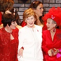 Mrs. Laura Bush in a white skirt suite with a Red Dress Pin in between Liza Minnelli and Rita Moreno who are both in red outfits, posing at the end of the 2008 fashion show.