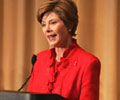 Mrs. Laura Bush wearing a red skirt suite speaks at a podium.