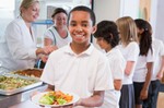 Schoolboy holding plate of lunch in school cafeteria smiling at camera