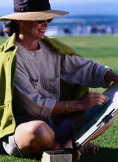 Fotografía de una mujer con sombrero y gafas de sol dibujando en el parque