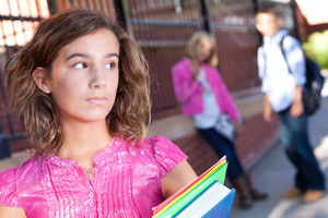 Photo shows a teenage girl walking alone in a schoolyard and glancing over her shoulder at a pair of teens behind her.