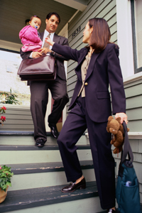 a woman in a business suit outside a house with a man holding a baby
