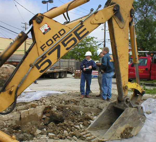 A backhoe digging in the ground and 3 people working