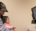 Photo of a 10-month-old baby held by a woman watching images on a monitor.