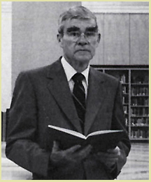 A black and white half length photograph John Blake in the History of Medicine Division reading room holding an open book in his hands.