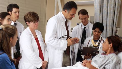 This is a photograph of a doctor and other hospital staff talking to a cancer patient lying in a hospital bed.