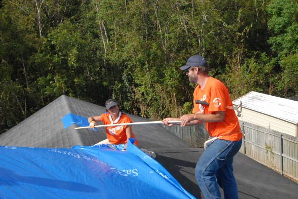 volunteers cover a roof with blue tarp