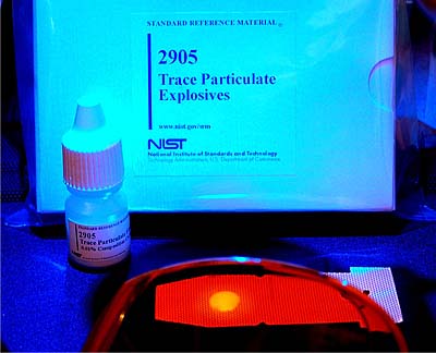 SRM 2905, Trace Particulate Explosive Simulants. Seen through a pair of specially filtered glasses under a blue crime-scene light, a spot of the fluorescently tagged SRM is plainly visible