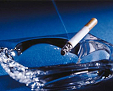 Lit cigarette lays in a glass ashtray.