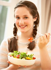 A girl smiles as she eats a salad.