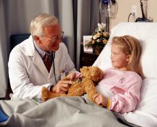 Photograph of a male doctor with his stethoscope on the teddy bear of a young female patient