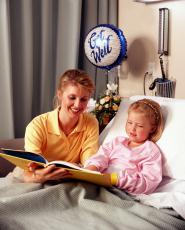 Photograph of a woman reading to a young girl in a hospital bed