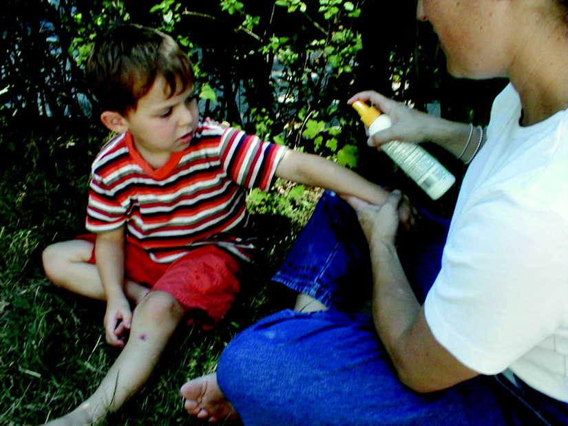 Parent carefully applying insect repellent spray to the exposed skin of their child.