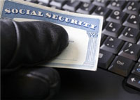 thief holding a social security card over a computer keyboard