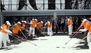 Photograph of people in orange shirts painting a black roof white.