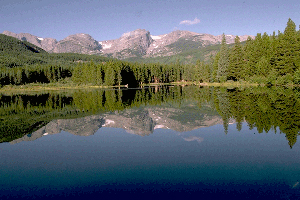 Photograph of a lake surrounded by evergreen trees and mountains.
