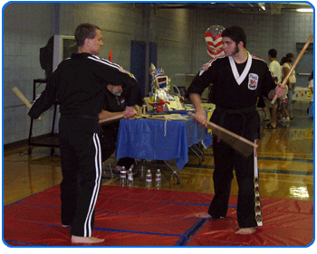 Two men in black athletic ensembles demonstrate karate moves together