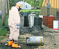 Disposal site with 55 gallon drums and workers in protective suits.