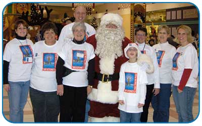 Seven adults and one child in matching t-shirts stand with Santa Claus at the mall